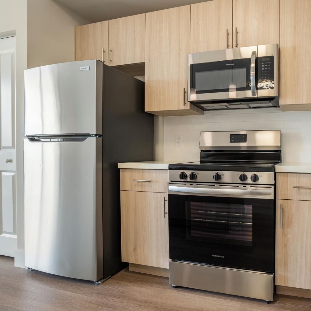 Northside Vistas apartments modern kitchen with stainless steel appliances, light wood cabinets, and a sleek wooden floor.
