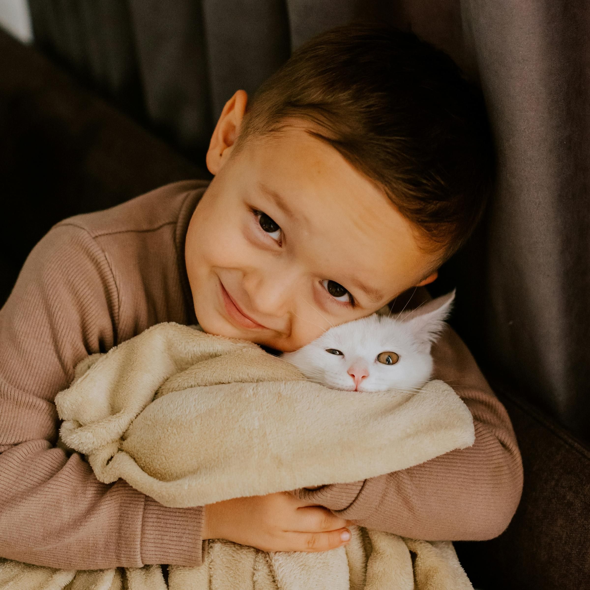 A smiling child hugs a white cat wrapped in a beige blanket on a couch at Northside Vistas apartments.