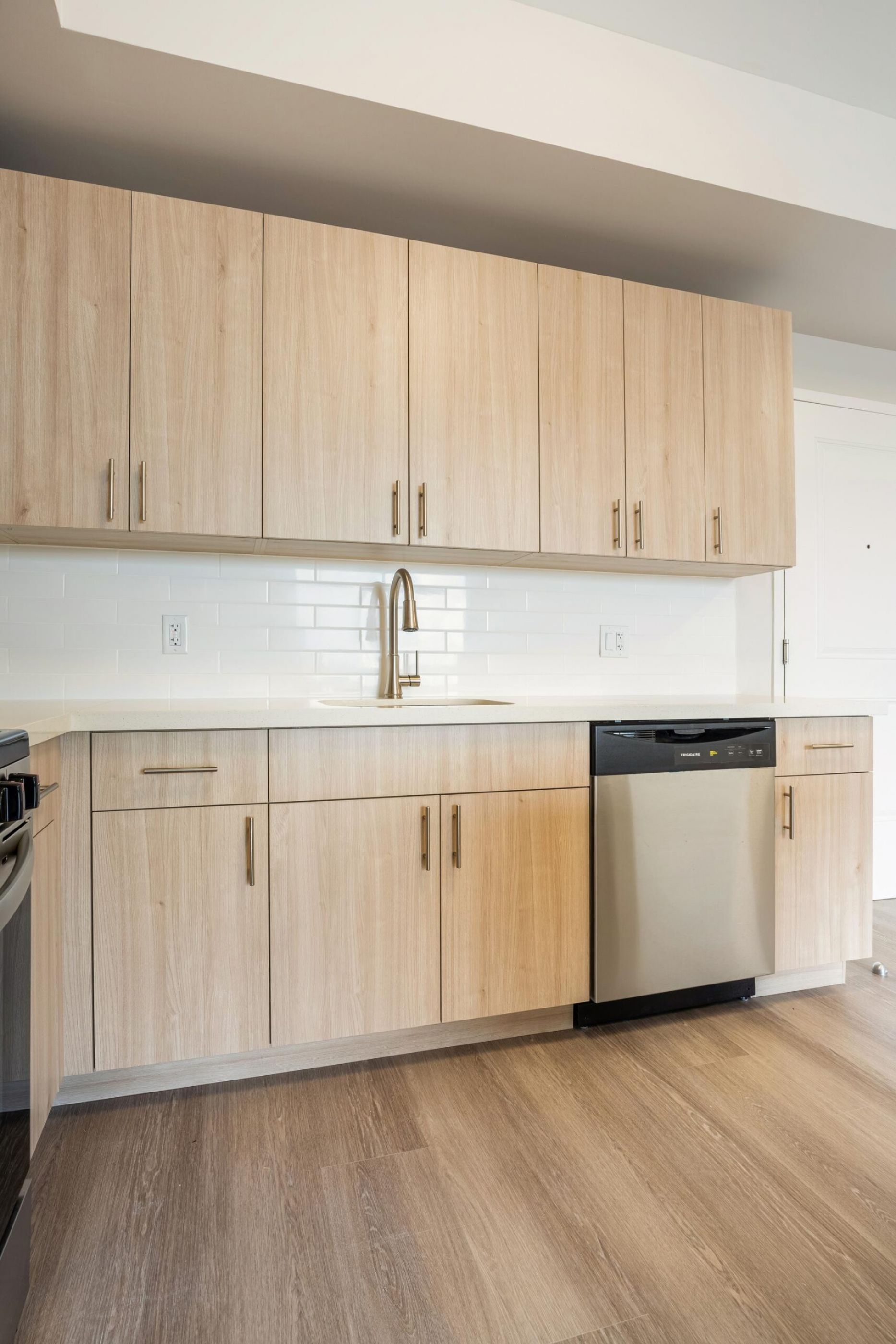 Northside Vistas apartments modern kitchen with light wood cabinets, white countertops, stainless steel dishwasher, and faucet.