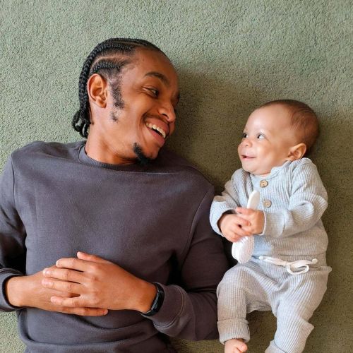 Northside Vistas apartments resident and baby lying on the floor, smiling at each other. The baby wears a gray outfit; the man wears a dark shirt.