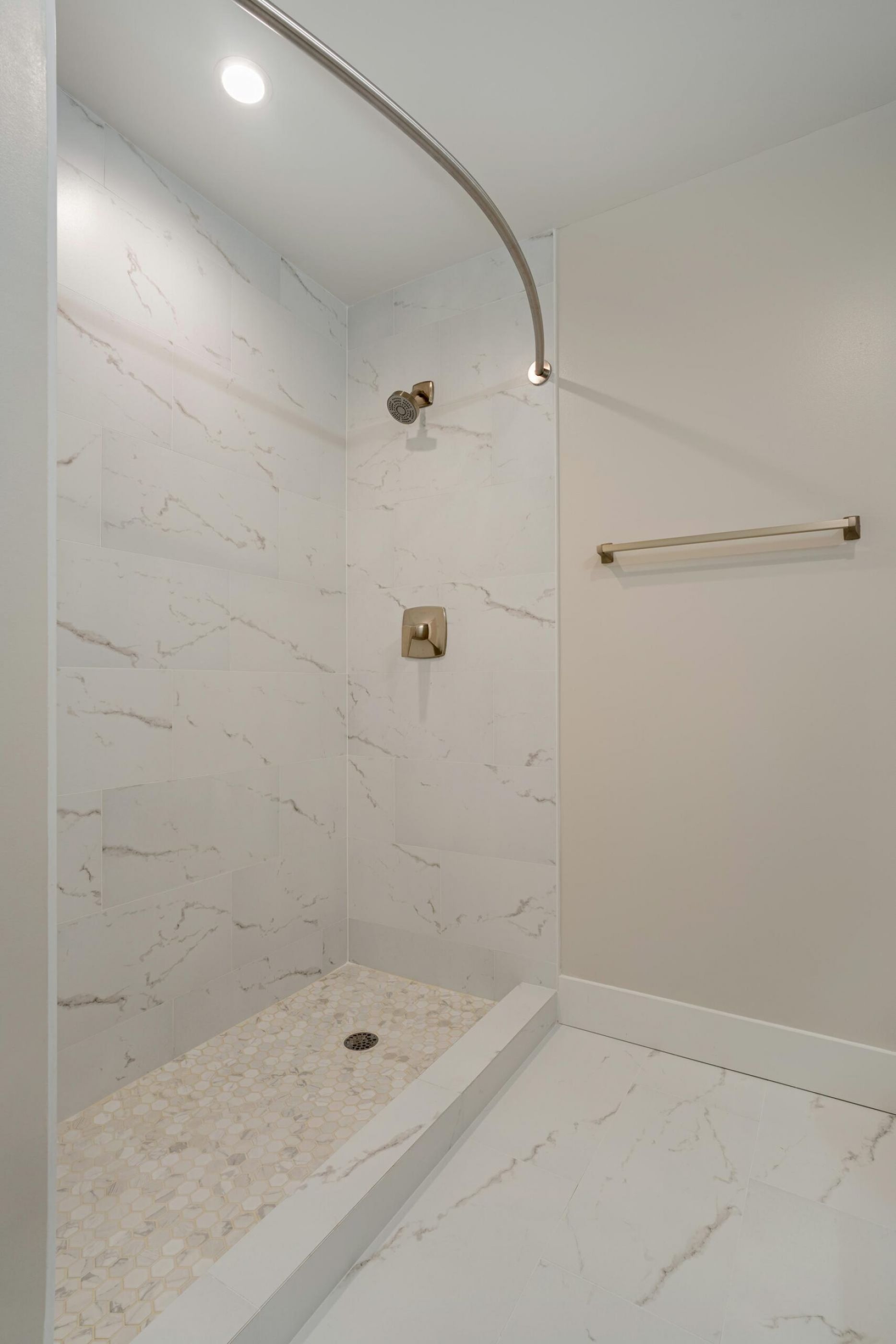 Northside Vistas apartments minimalist white marble shower with a curved curtain rod, gold fixtures, and a towel bar.