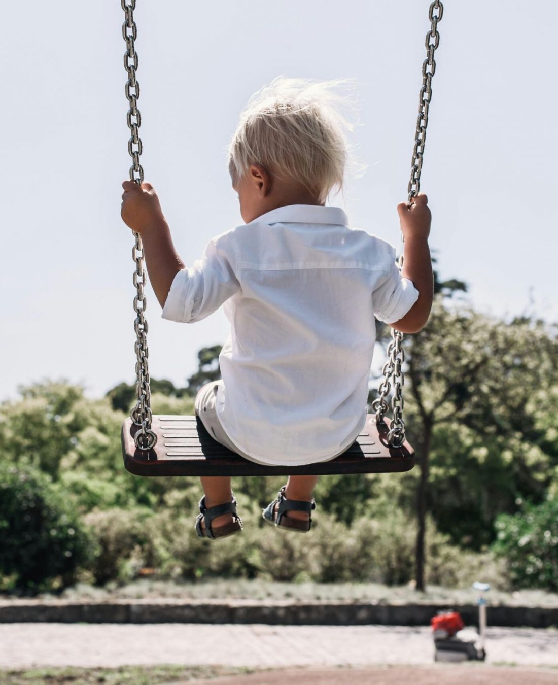 Child in white shirt swinging in a park, facing away, with trees in the background near Northside Vistas apartments.